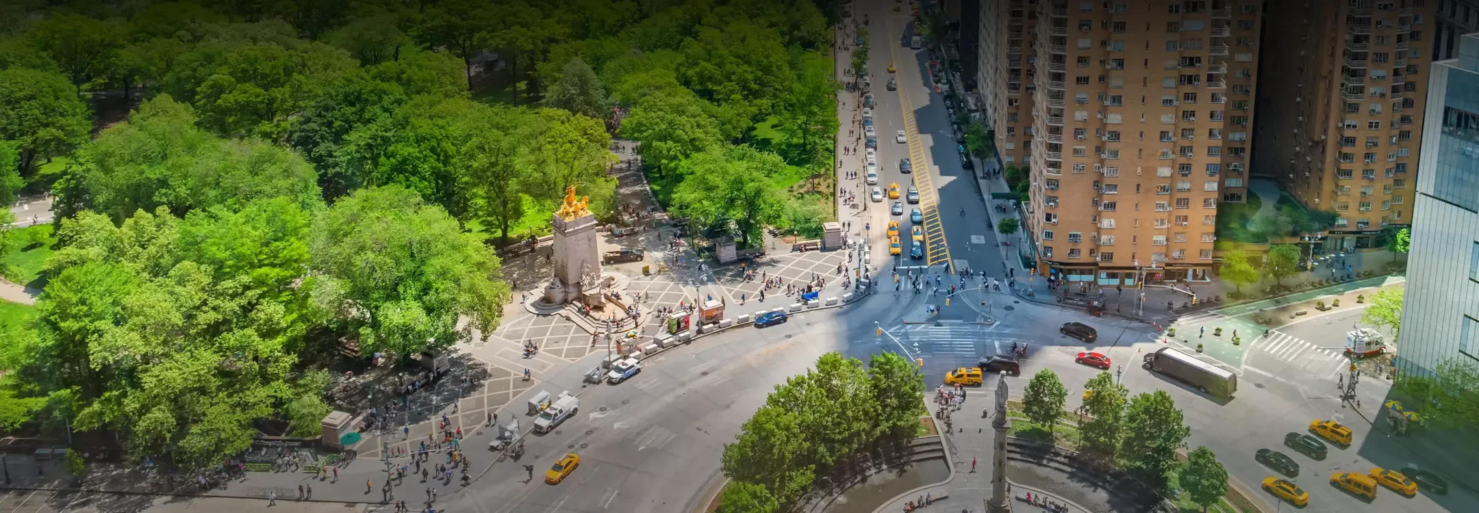 Aerial view of a bustling intersection near Helena 57 West, with taxis and pedestrians adjacent to green park spaces.