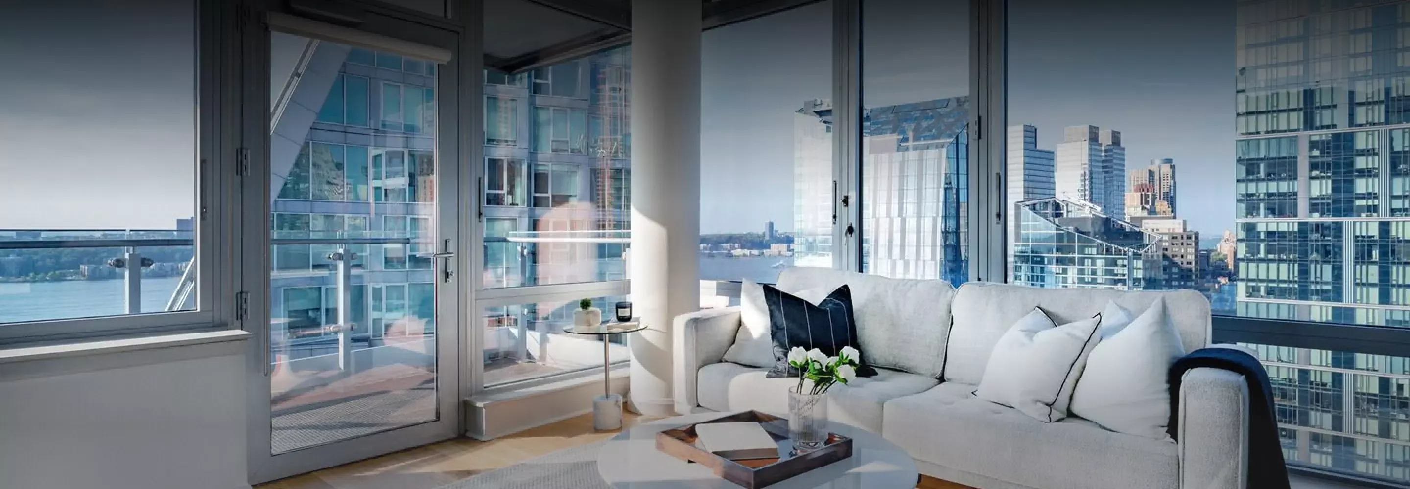 Spacious living area within Helena 57 West, bathed in natural light, with a plush sofa and sweeping views of the waterfront through floor-to-ceiling windows.